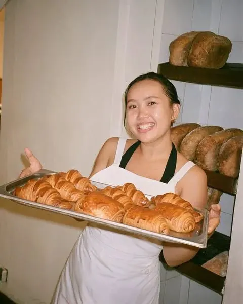Emma holding a tray of freshly baked croissants in her bakery